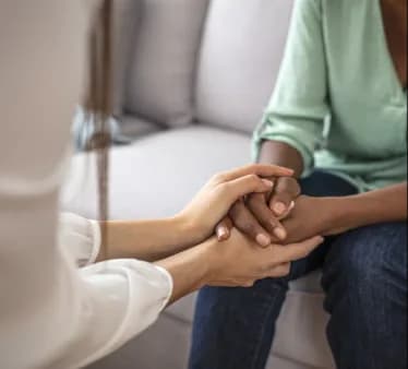 Duas pessoas sentadas, de mãos dadas, durante um momento de acolhimento.